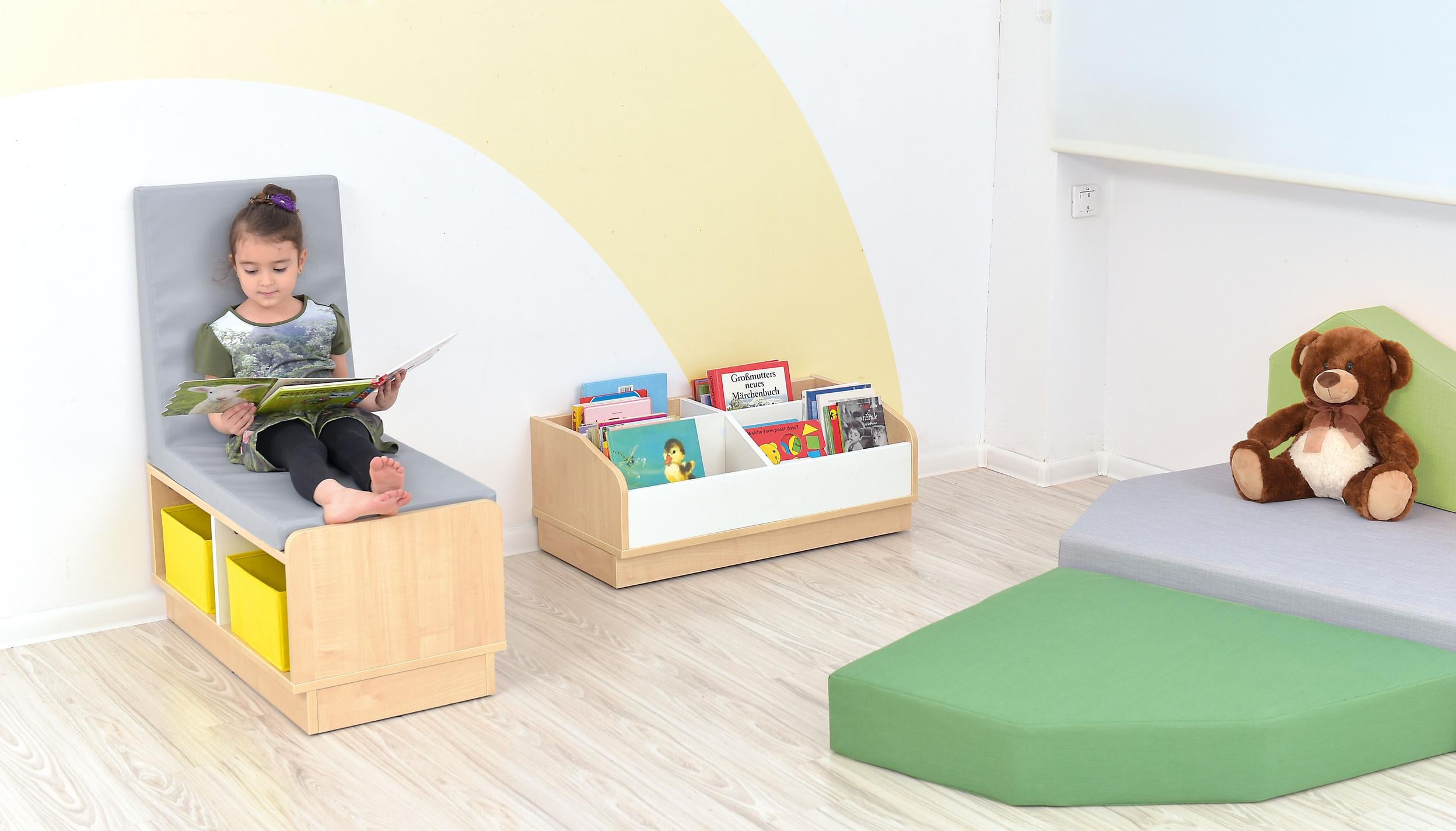 Kind liest auf Sitzbank mit Regal in Leseecke. - Produkt wird im Kindergarten oder Schule genutzt.