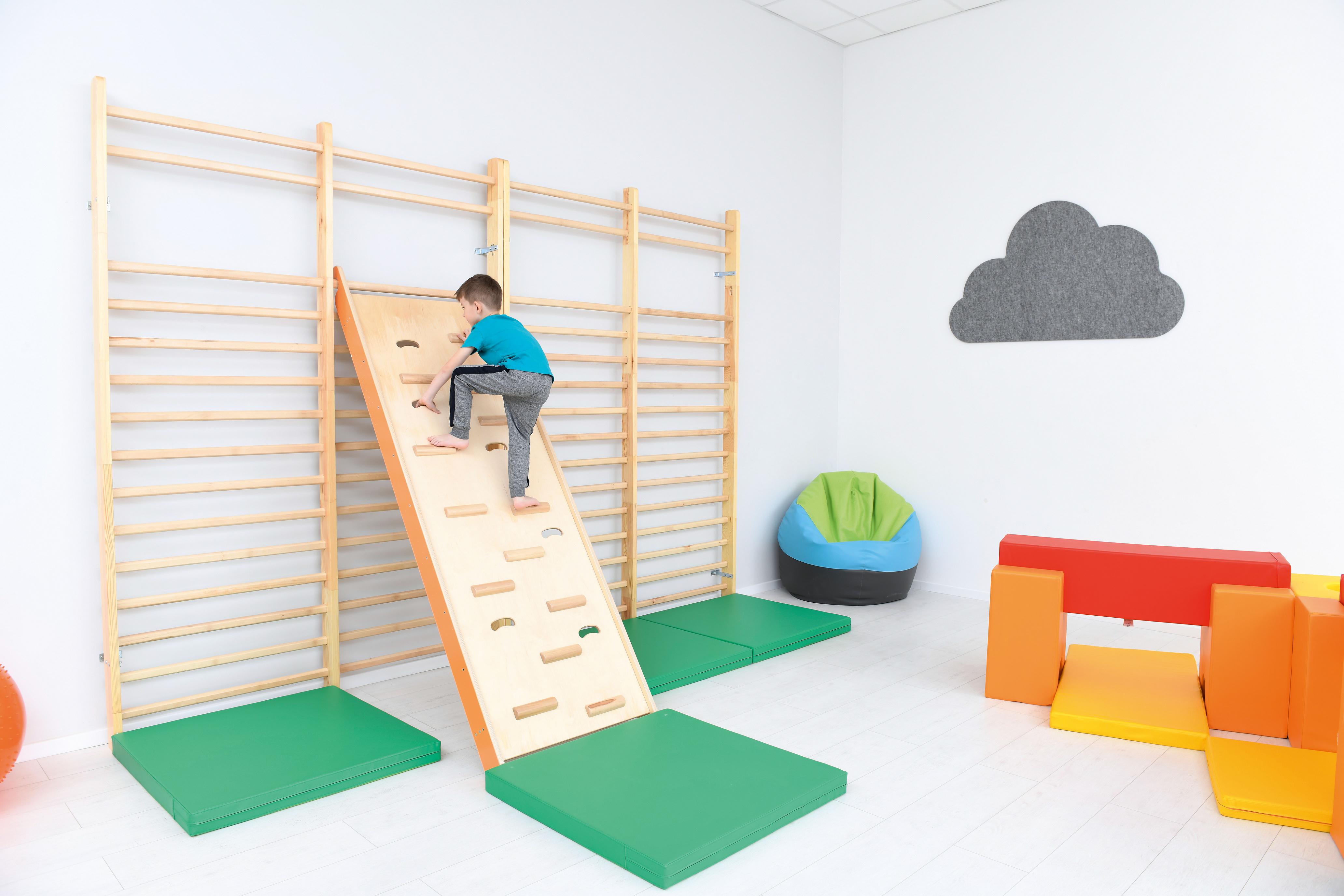 Kind klettert an Sprossenwand, Kita-Bewegungsspielzeug sichtbar.