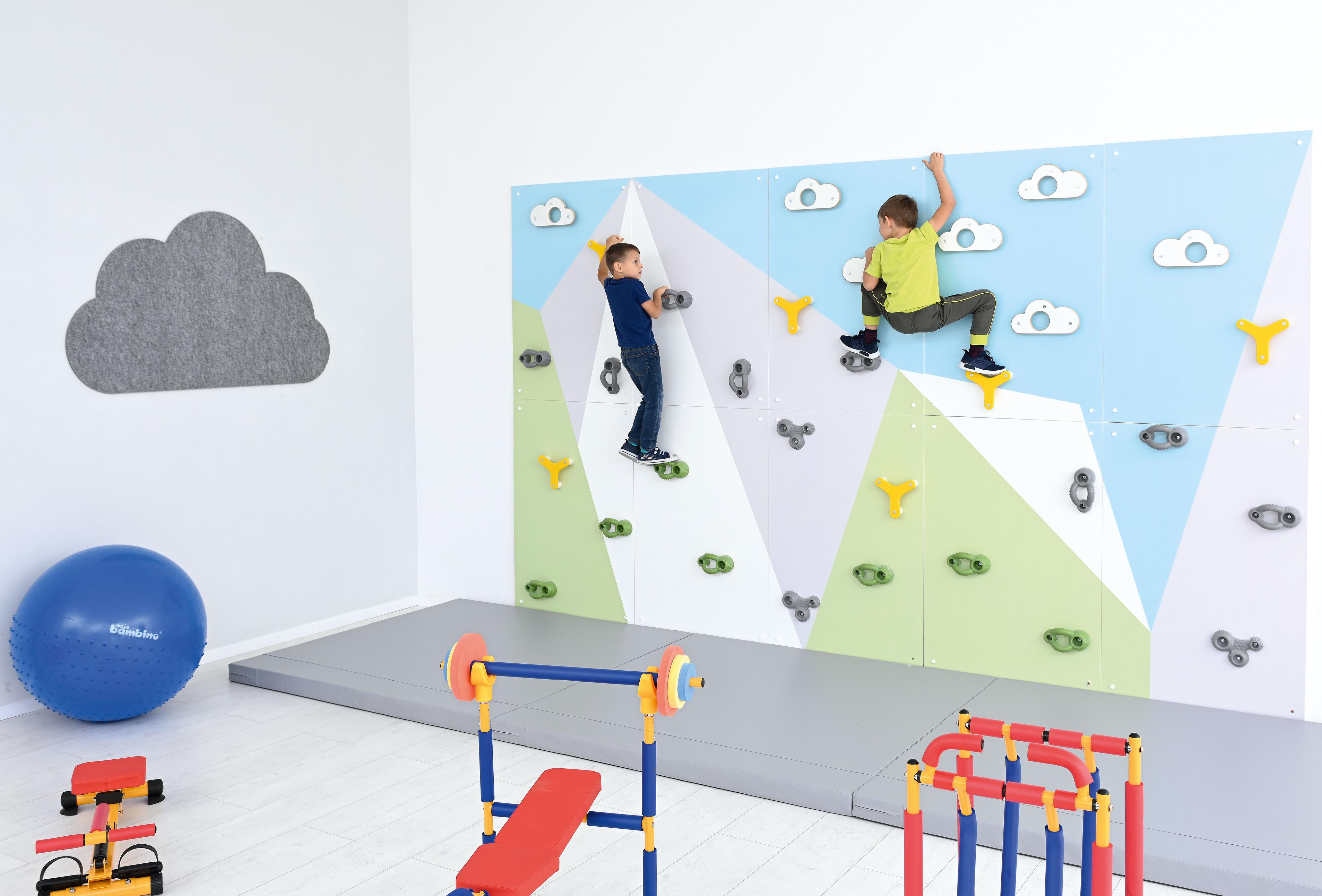 Kinder klettern an bunter Kletterwand in Sporthalle.