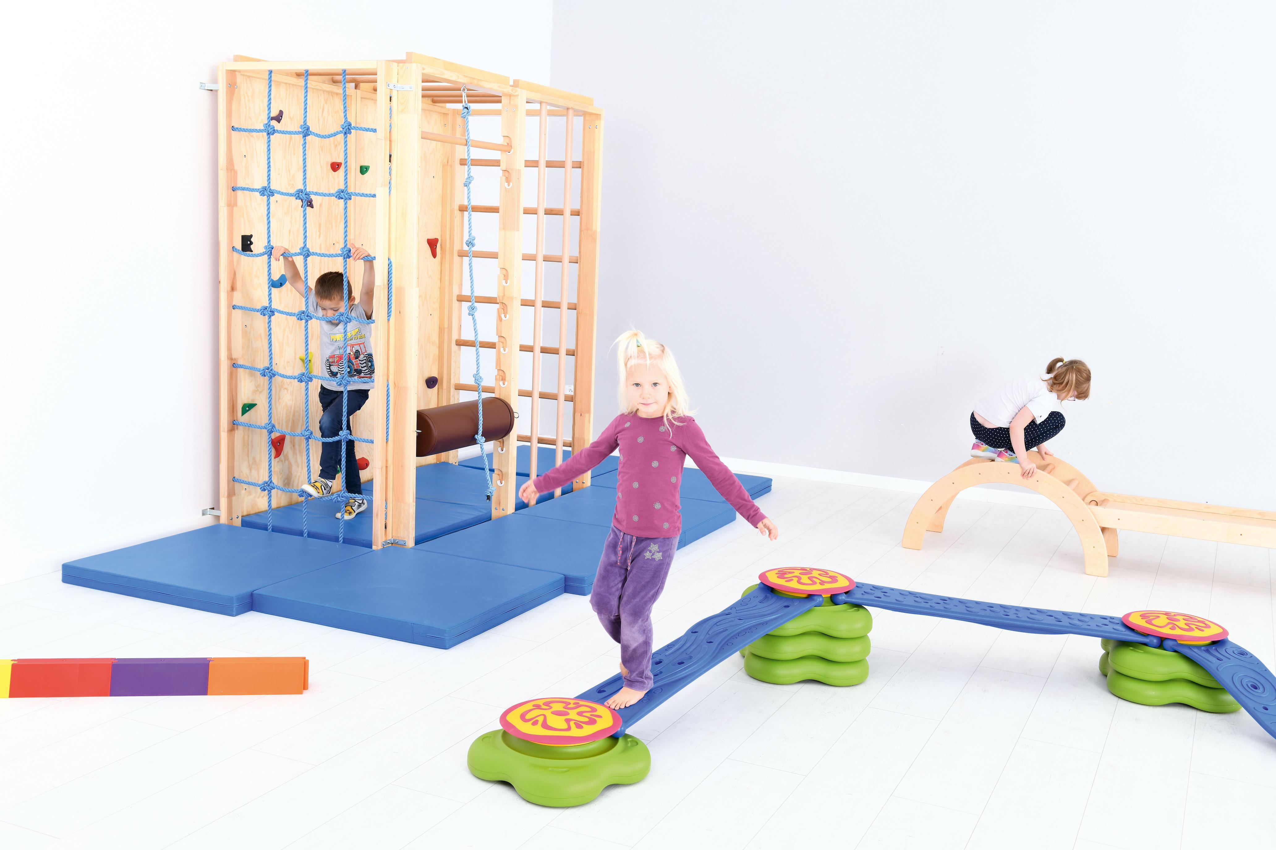 Kinder spielen auf Turnhalle-Kletterwand und Balance-Spielzeug.