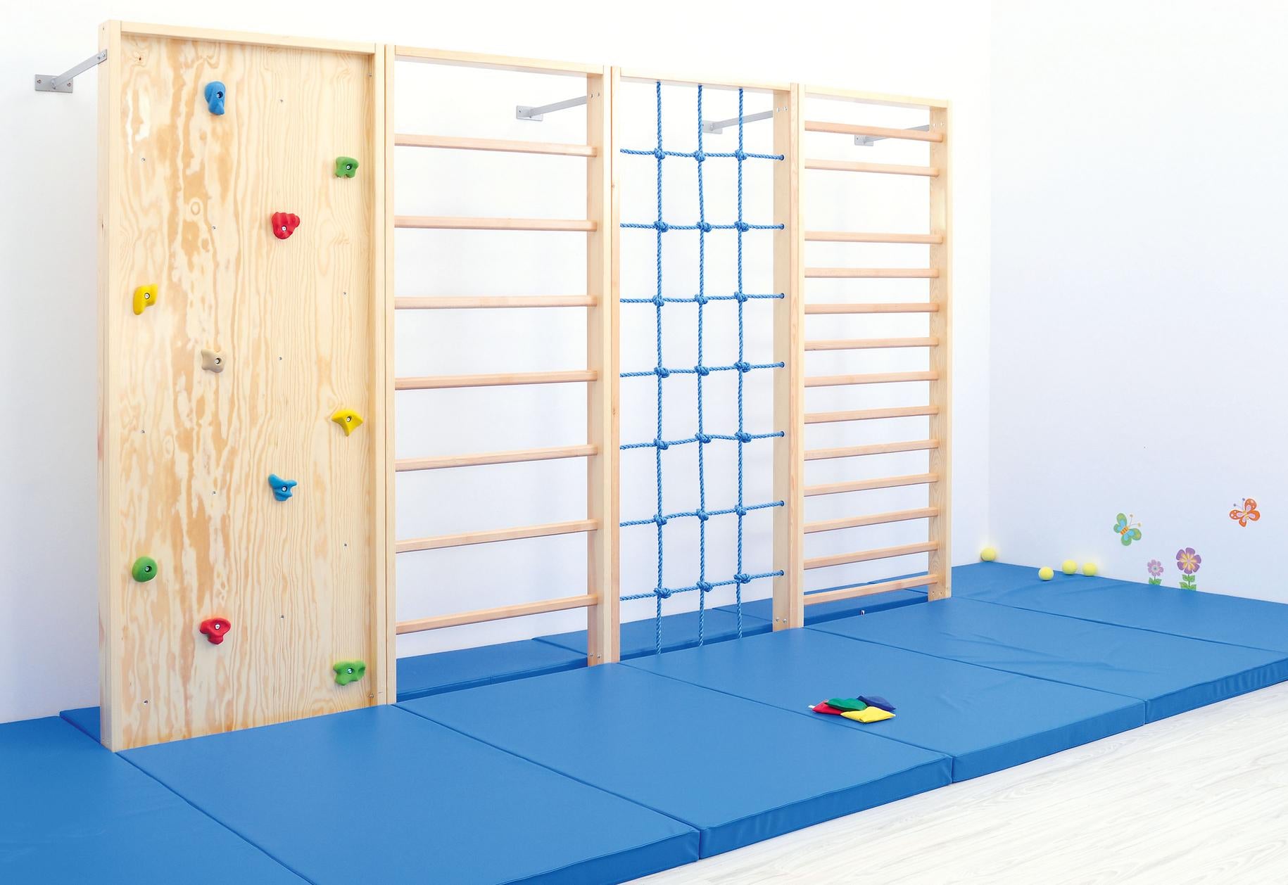 Kletterwand in Turnhalle mit blauen Matten darunter.