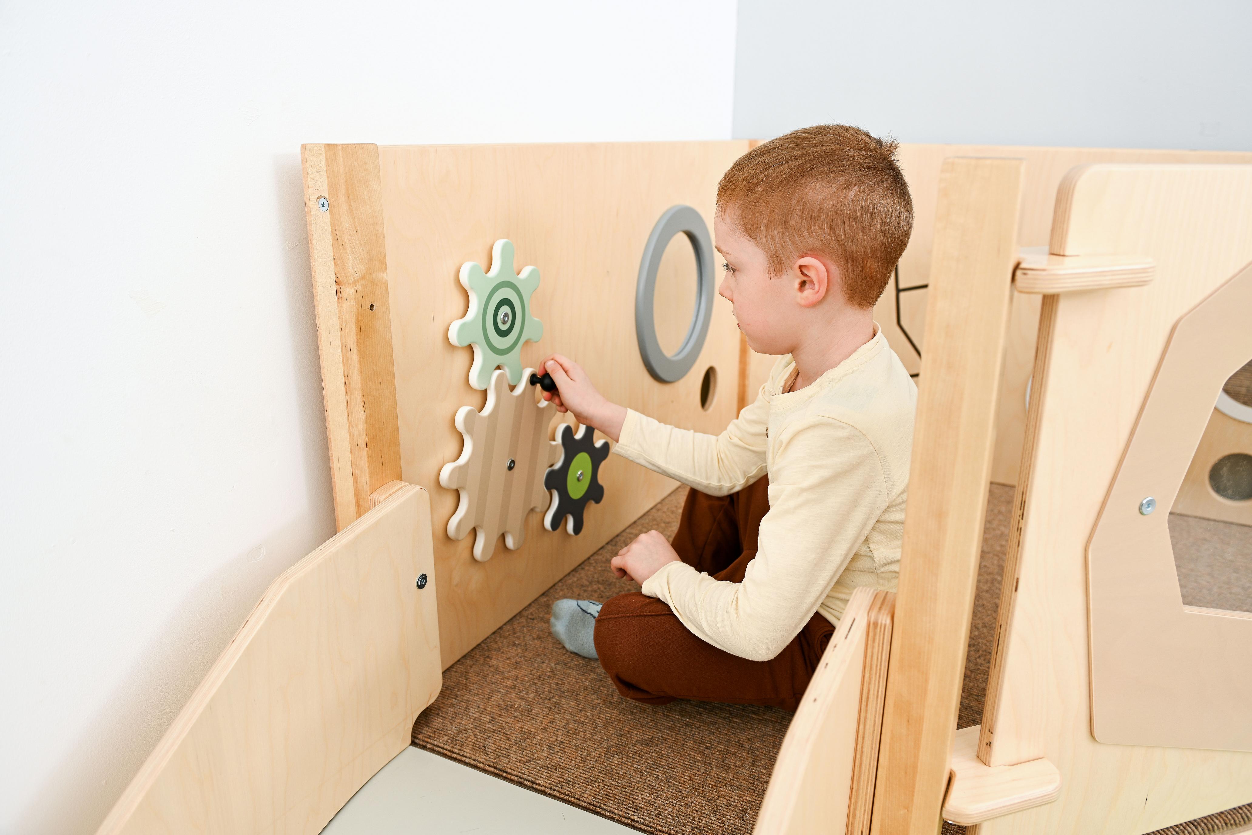 Sensorische Spielecke: Kind entdeckt hölzernes Spielmodul oben.