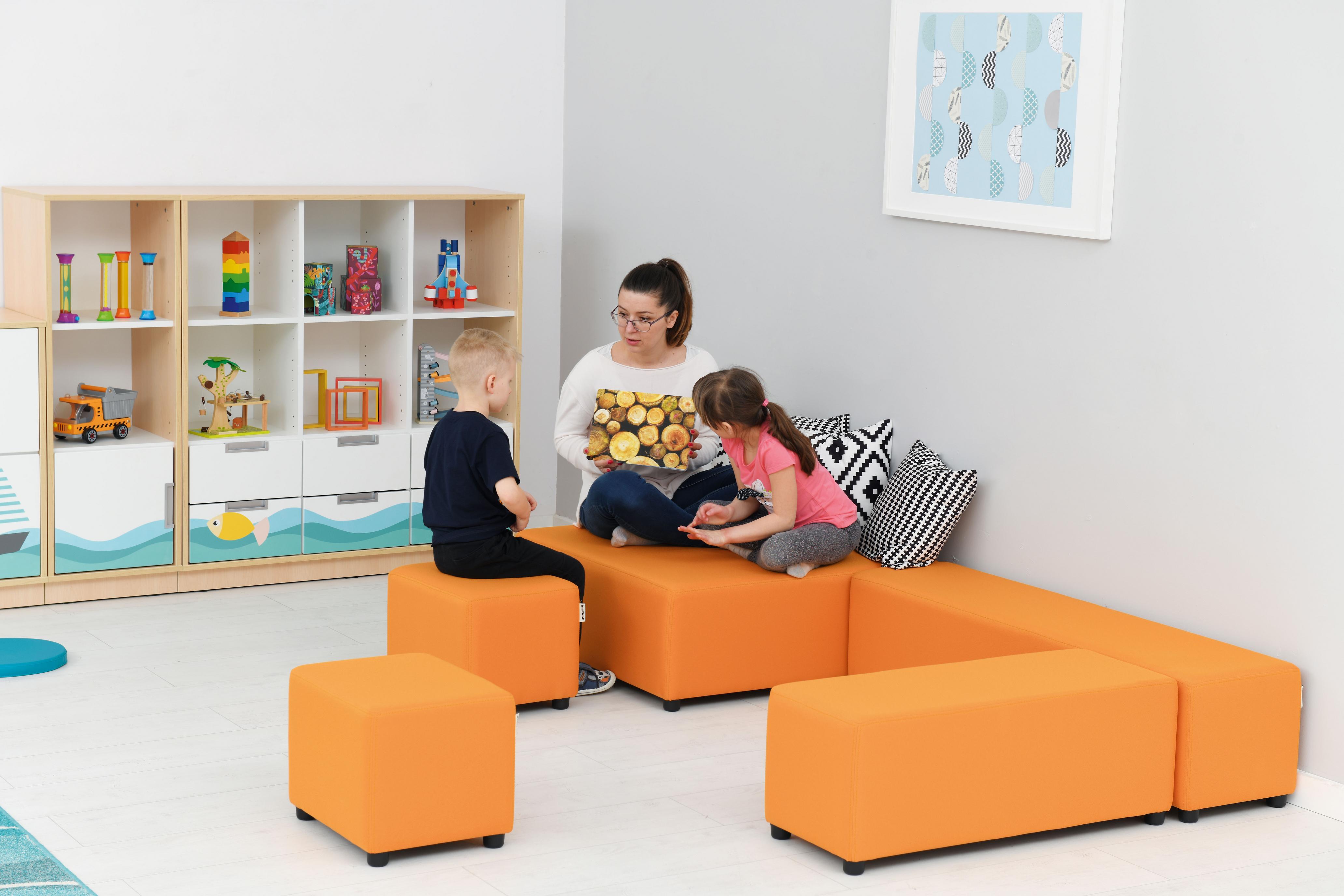Kinder und Betreuer sitzen auf orangenen Loungemöbeln.
